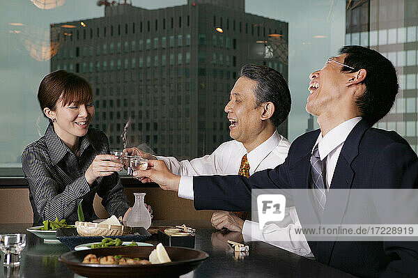 Glückliche Geschäftsleute stoßen in einem Hochhausrestaurant mit Sake an