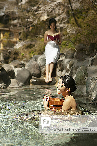 Glückliche junge Frauen entspannen am sonnigen Pool in Onsen