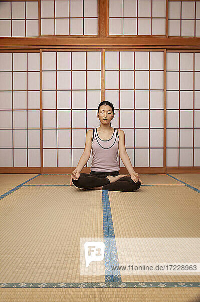 Serene junge Frau meditiert in Lotus-Pose auf Matte