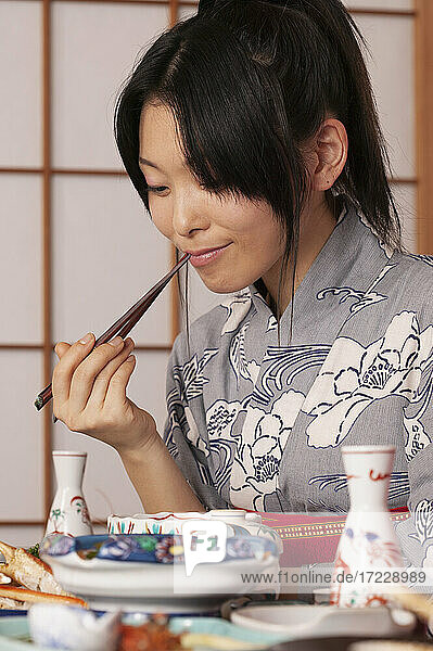 Junge Frau im Kimono isst traditionelle japanische Mahlzeit mit Stäbchen