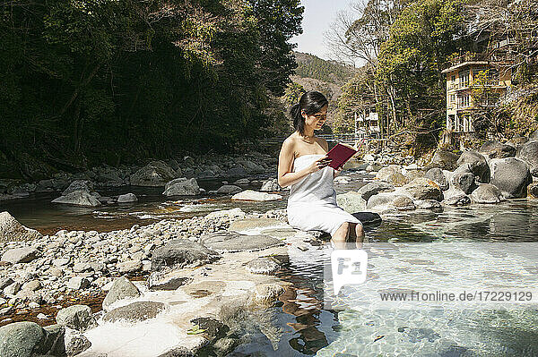 Junge Frau im Handtuch liest Buch am sonnigen Pool im Onsen  Izu  Japan