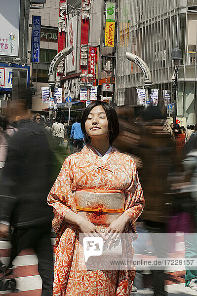 Serene young woman in kimono in sunny bustling city street  Kyoto  Japan