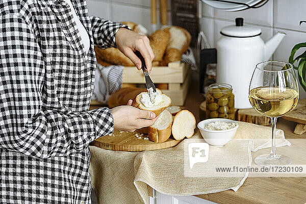 Frau in der Küche macht Sandwiches mit Baguette und Frischkäse