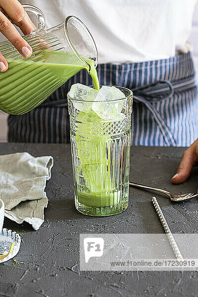 Woman pours matcha tea into a glass with ice cubes