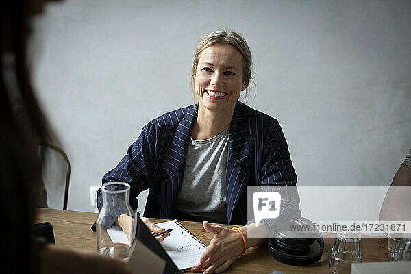 Smiling businesswoman discussing with colleague at desk in creative office