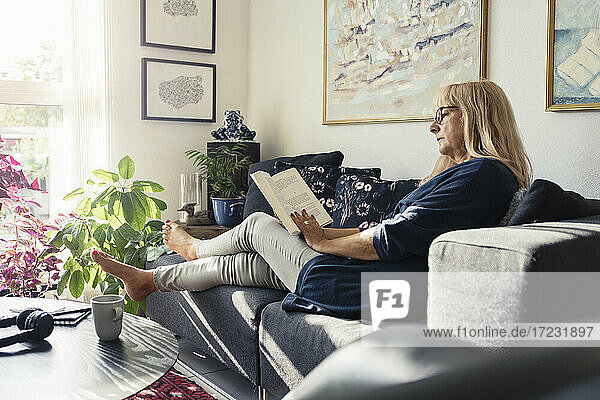 Blonde Frau liest Buch  während sie auf dem Sofa im Wohnzimmer sitzt