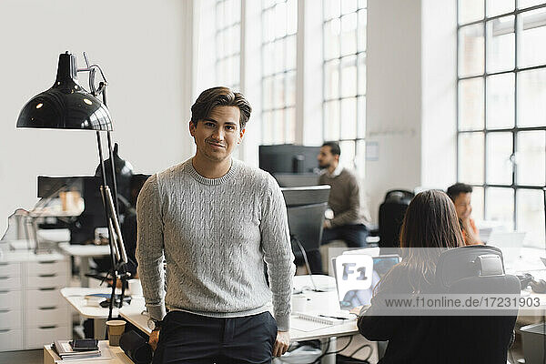 Portrait of male entrepreneur leaning on desk in office