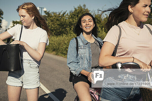 Lächelnde Freundinnen mit Fahrrad auf der Straße während des sonnigen Tages