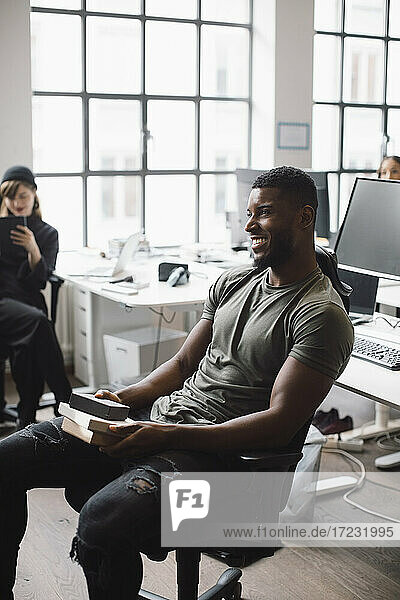 Lächelnde männliche Unternehmer mit Produkt sitzen auf Stuhl im Büro