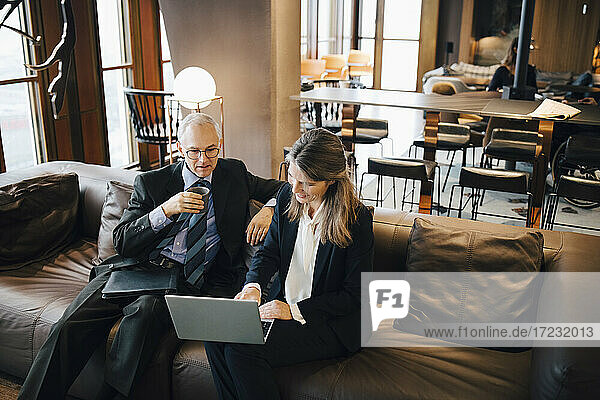 Männliche und weibliche Unternehmer diskutieren über Laptop beim Kaffee in der Cafeteria