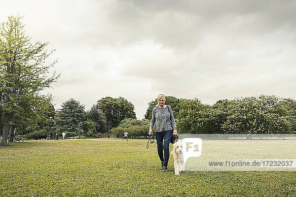 Mature woman walking with dog in park against sky