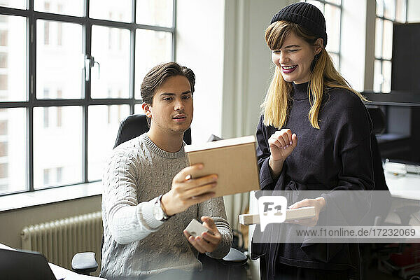 Smiling female entrepreneur discussing over product with male colleague at creative office