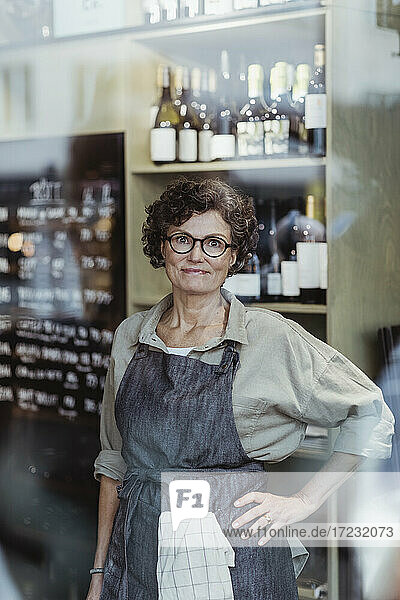 Portrait of smiling female store owner with hand on hip at deli store