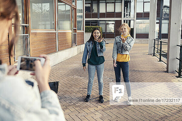 Teenager-Mädchen  das lächelnde Freundinnen auf dem Fußweg vor einem Gebäude fotografiert