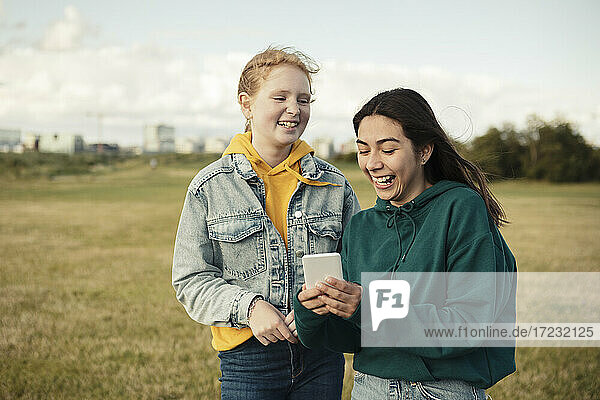 Fröhliche weibliche Freunde lachend bei der Verwendung von Smartphone im Park