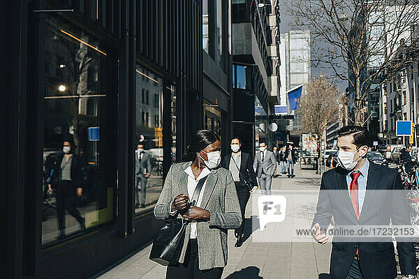 Männliche und weibliche Kollegen diskutieren beim Spaziergang an einem sonnigen Tag in der Stadt während COVID-19