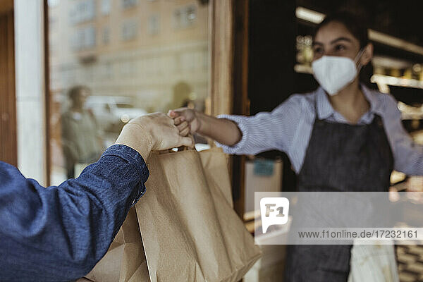 Verkäuferin gibt Kunden im Feinkostladen während der Pandemie Essen zum Mitnehmen