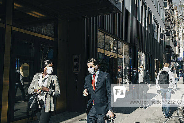 Geschäftsmann mit weiblicher Kollegin im Gespräch beim Gehen auf dem Fußweg in der Stadt während der Pandemie