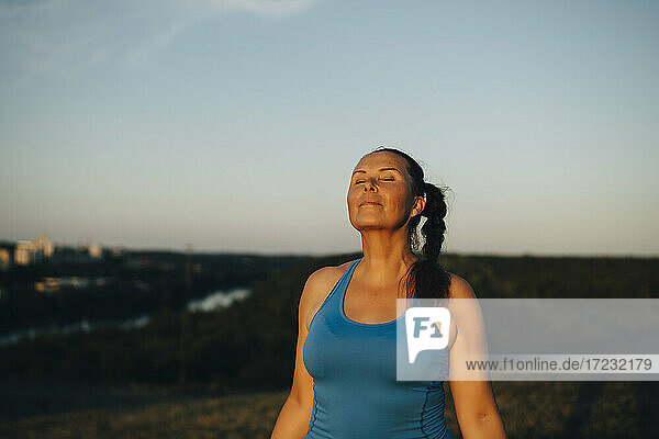 Weibliche Athletin mit geschlossenen Augen gegen den Himmel bei Sonnenuntergang