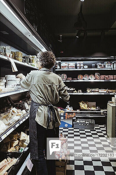 Rear view of female owner arranging product on rack at delicatessen shop
