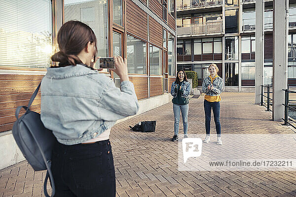 Teenager-Mädchen  das seine Freundinnen fotografiert  während es auf dem Fußweg vor einem Gebäude steht
