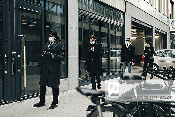 Geschäftsleute  die soziale Distanz wahren  während sie auf dem Fußweg bei einem Gebäude in der Stadt stehen