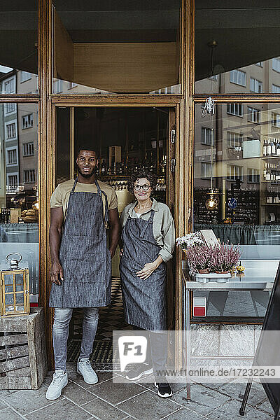 Portrait of male and female colleagues at doorway of delicatessen shop