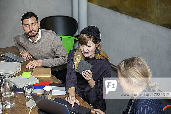 Geschäftsfrau mit Laptop während der Diskussion mit männlichen und weiblichen Kollegen im kreativen Büro