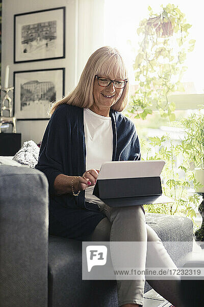 Lächelnde Frau mit digitaler Tablette beim Sitzen auf dem Sofa zu Hause