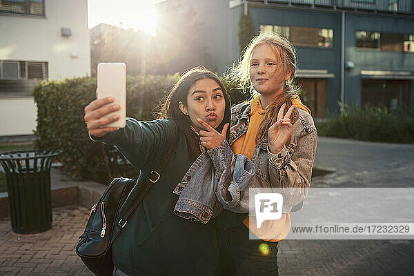 Weibliche Freunde gestikulieren  während sie ein Selfie über Smartphone auf dem Fußweg machen