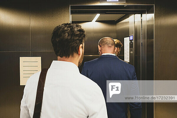 Rear view of business people walking inside elevator