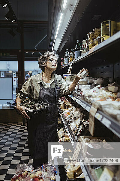 Female owner arranging product on rack at delicatessen store