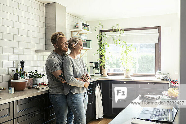 Mann umarmt Frau  während er in der Küche zu Hause steht