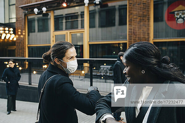 Weibliche Kollegen grüßen mit Ellenbogenstoß auf dem Fußweg in der Stadt während COVID-19