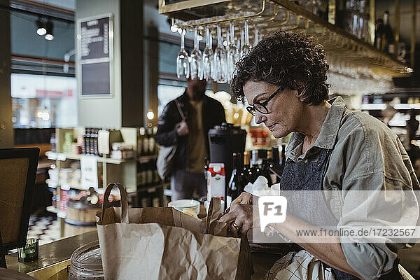 Female owner packing order in paper bag at delicatessen shop