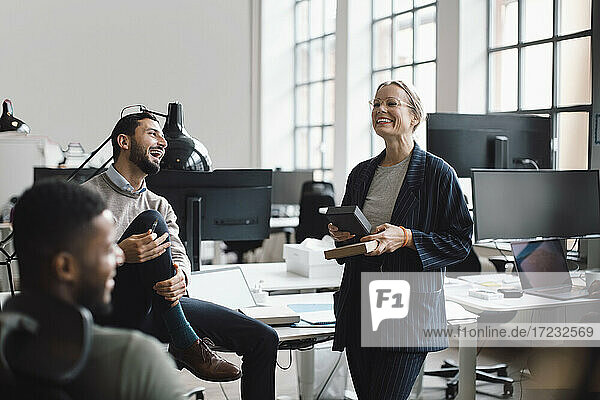 Happy female and male colleagues discussing over product in office