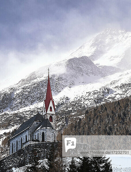 Kirche mit einem schneebedeckten Berge im Hintergrund mit Windböen an den Hängen und oben  Trentino-Südtirol  Italien  Europa