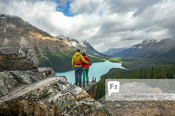 Paar umarmt sich  blickt in die Ferne  Ausblick auf türkisfarbenen Gletschersee umgeben von Wald  Peyto Lake  Rocky Mountains  Banff-Nationalpark  Provinz Alberta  Kanada  Nordamerika
