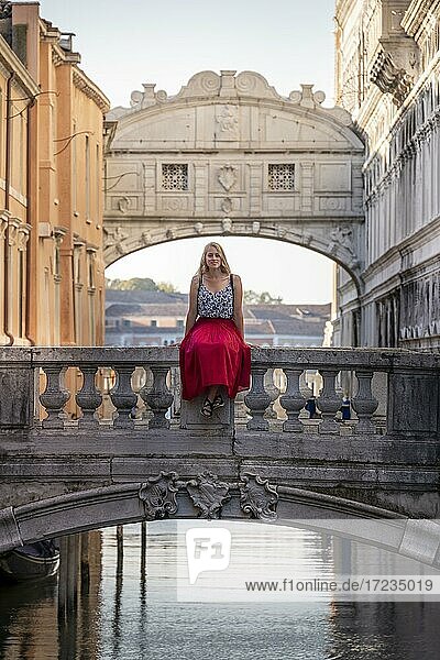 Junge Frau mit rotem Rock  Touristin sitzt auf einer Brückengeländer  Brücke über dem Rio di Palazzo  hinten Seufzerbrücke  Venedig  Venetien  Italien  Europa