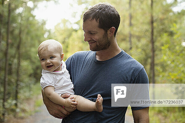 Happy mid adult man carrying baby daughter on forest track