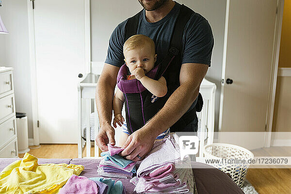 Mid adult man doing chores with baby daughter in baby sling
