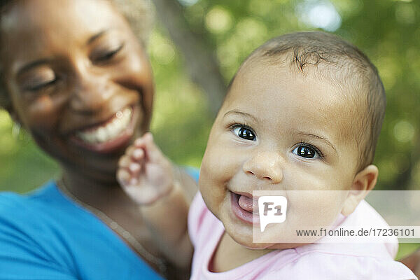 Kopf und Schultern der Mutter hält Baby-Mädchen Blick auf die Kamera lächelnd