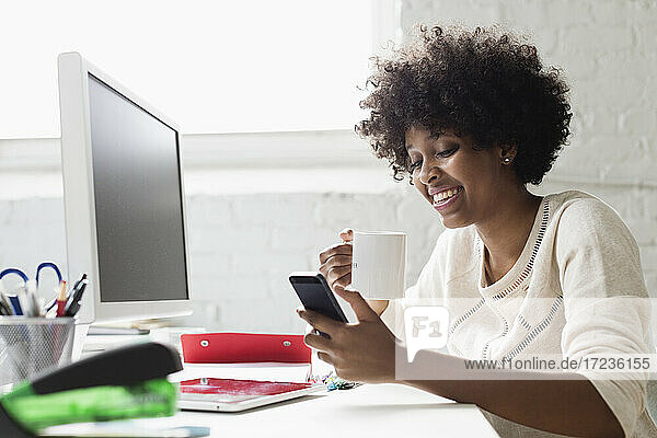 Young woman at desk with coffee using smartphone