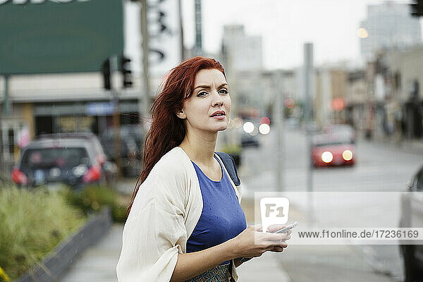Young woman with long red hair  using smartphone in street