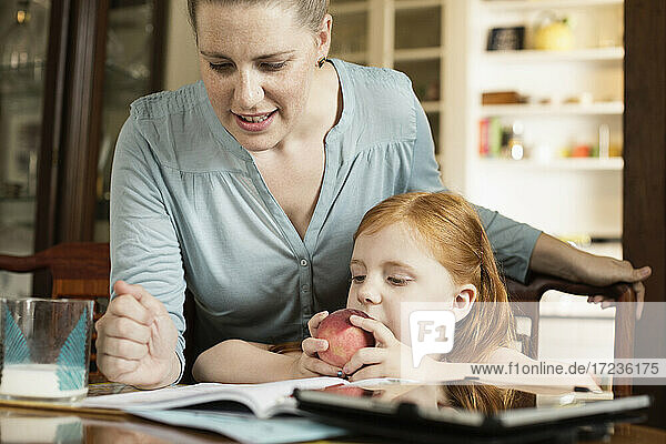 Mid erwachsene Mutter hilft Tochter bei den Hausaufgaben am Esszimmertisch