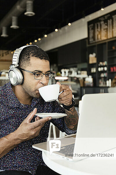 Young man in coffee shop  drinking coffee  using laptop