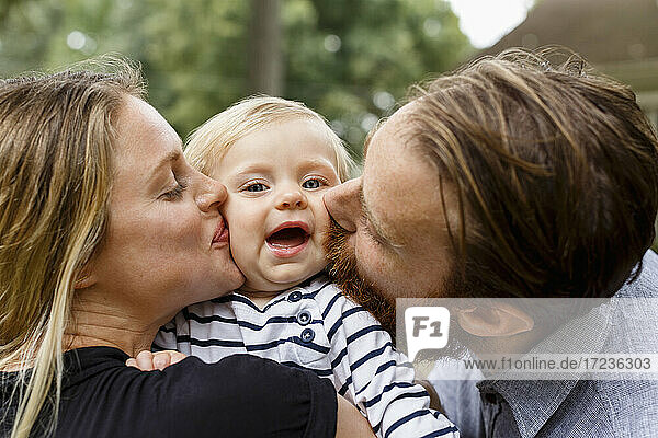 Mother and father kissing baby girl on cheek  outdoors