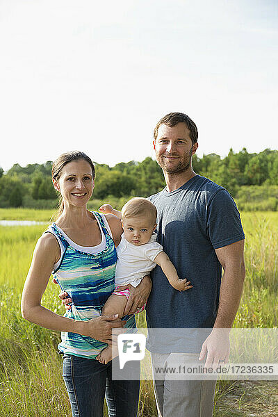 Portrait of mid adult parents carrying baby daughter by rural field