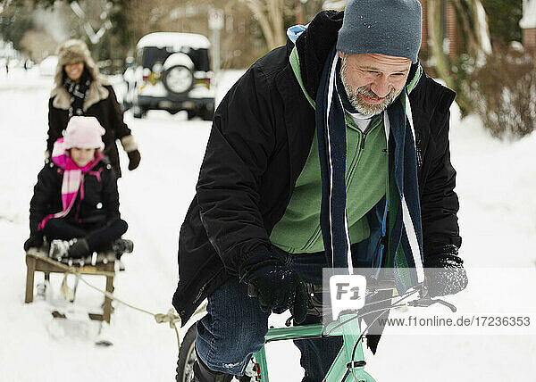 Eltern und Tochter spielen mit Schlitten im Schnee