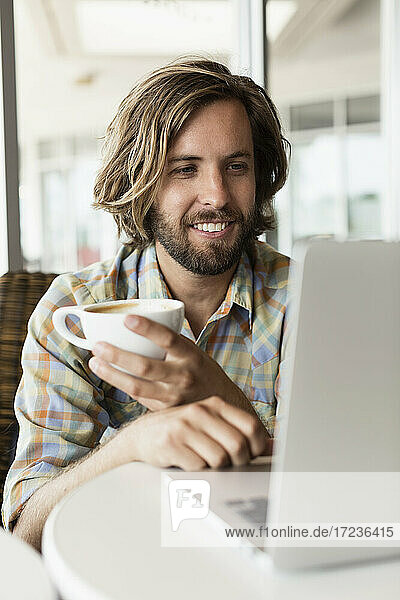 Mid adult man in coffee shop  drinking coffee  using laptop